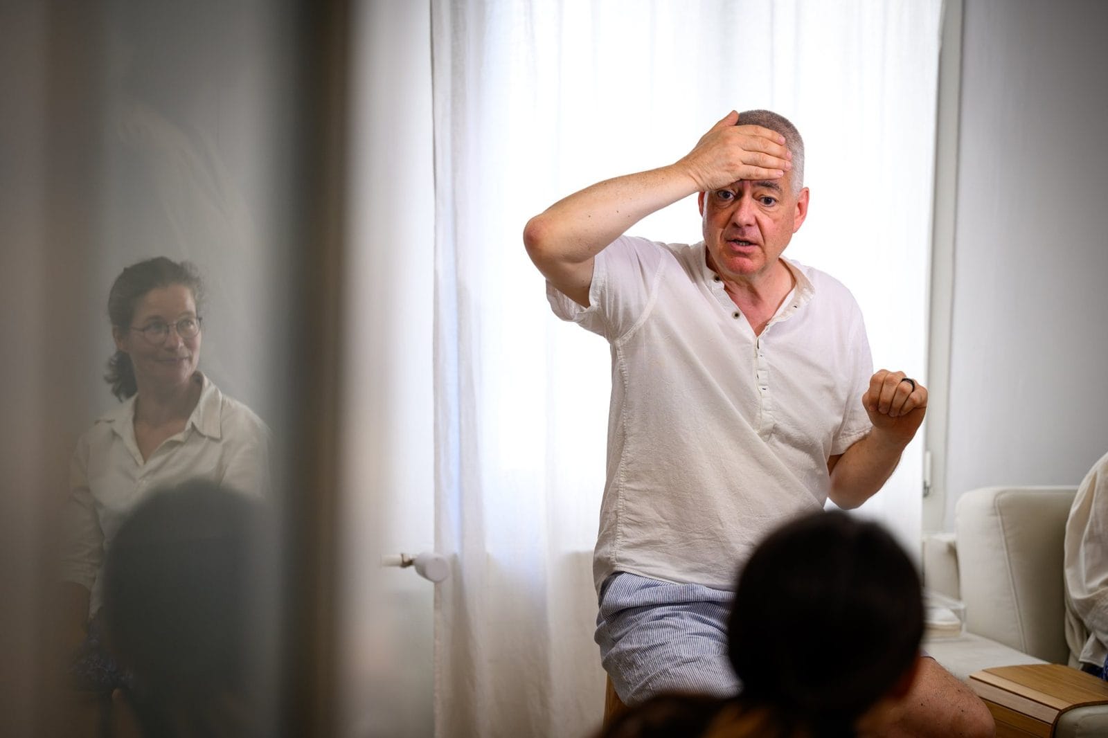 Mann in weissem Hemd fasst sich an die Stirn, Teilnehmende im Vordergrund